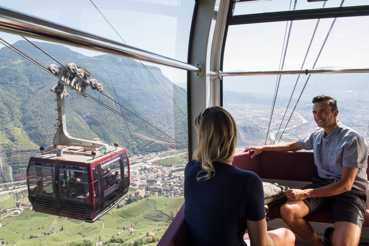 Ein Mann und eine Frau in der Gondel mit Blick auf die Stadt Bozen von oben