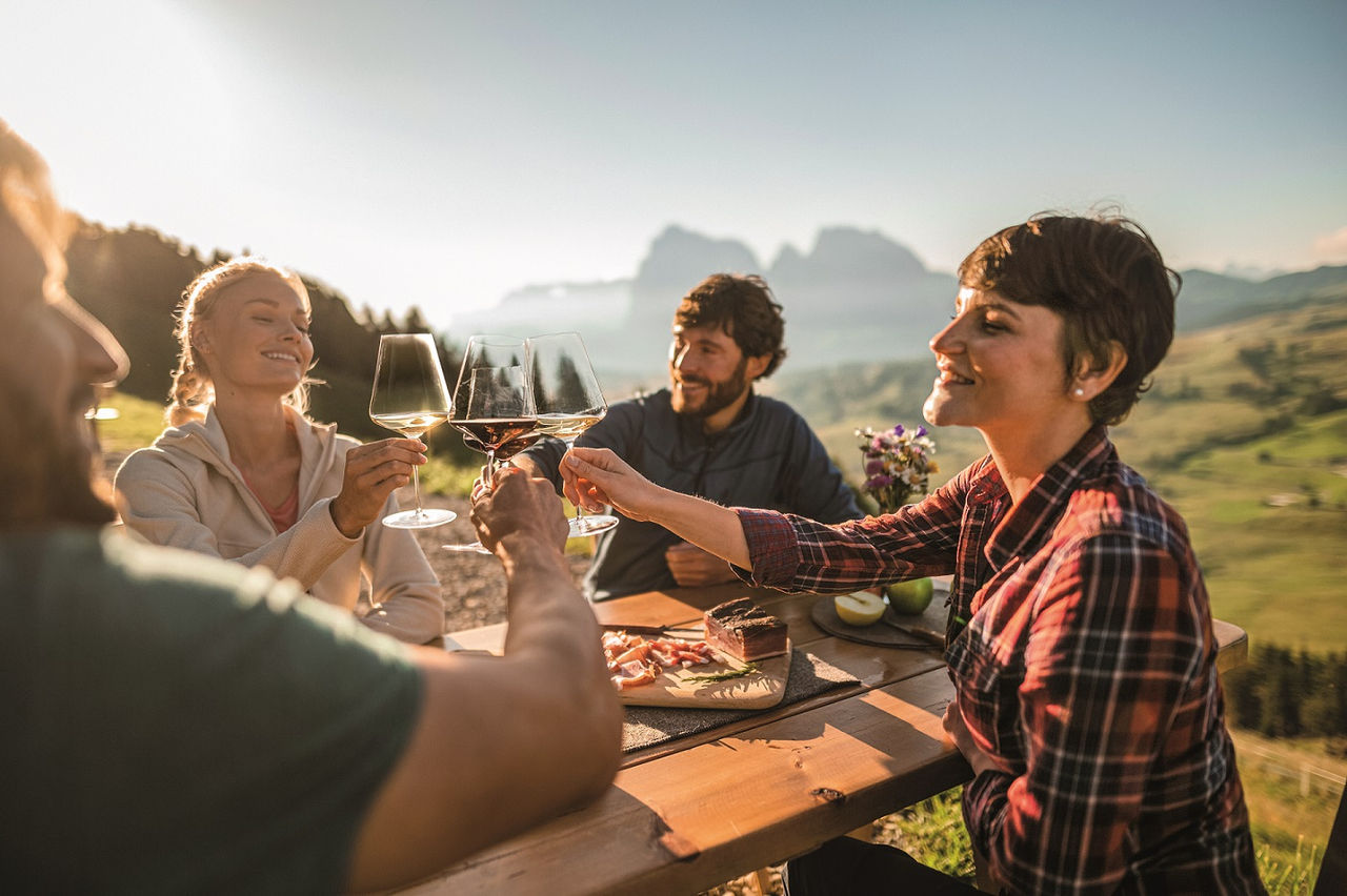 Freunde sitzen zusammen im freien an einem Tisch und stoßen mit einem Glas Wein an