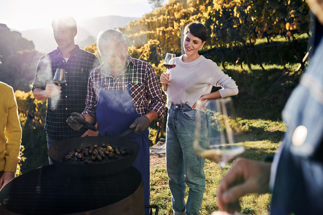 Un gruppo di persone prepara le caldarroste e beve del vino