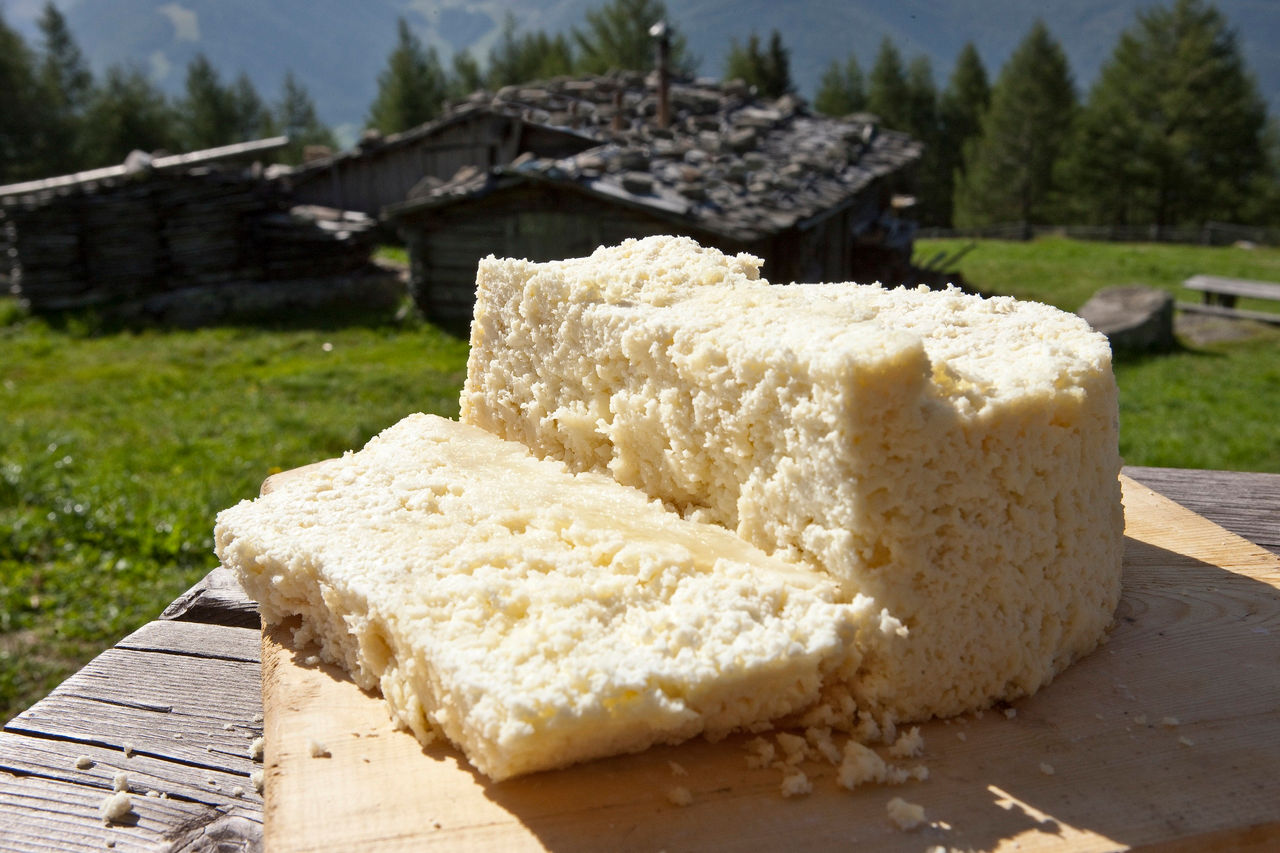 Ein Laib Graukäse auf einem Holzbrett mit urigen Holzhütten im Hintergrund